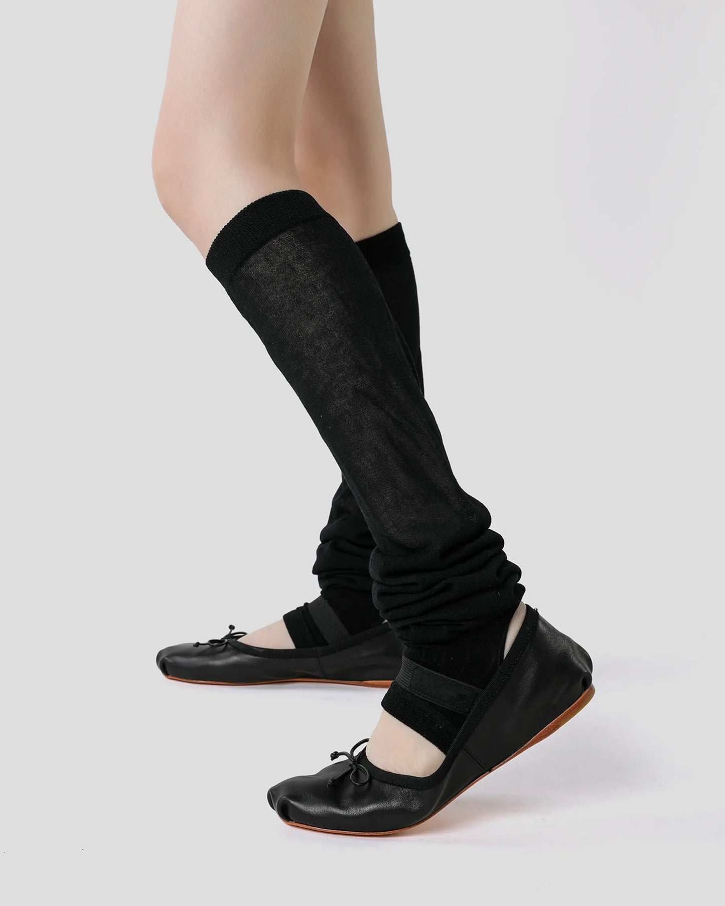 black | 03 | Black ballet stirrup leg warmers side standing view styled with black ballet flats, showing the gathered calf silhouette and stirrup construction