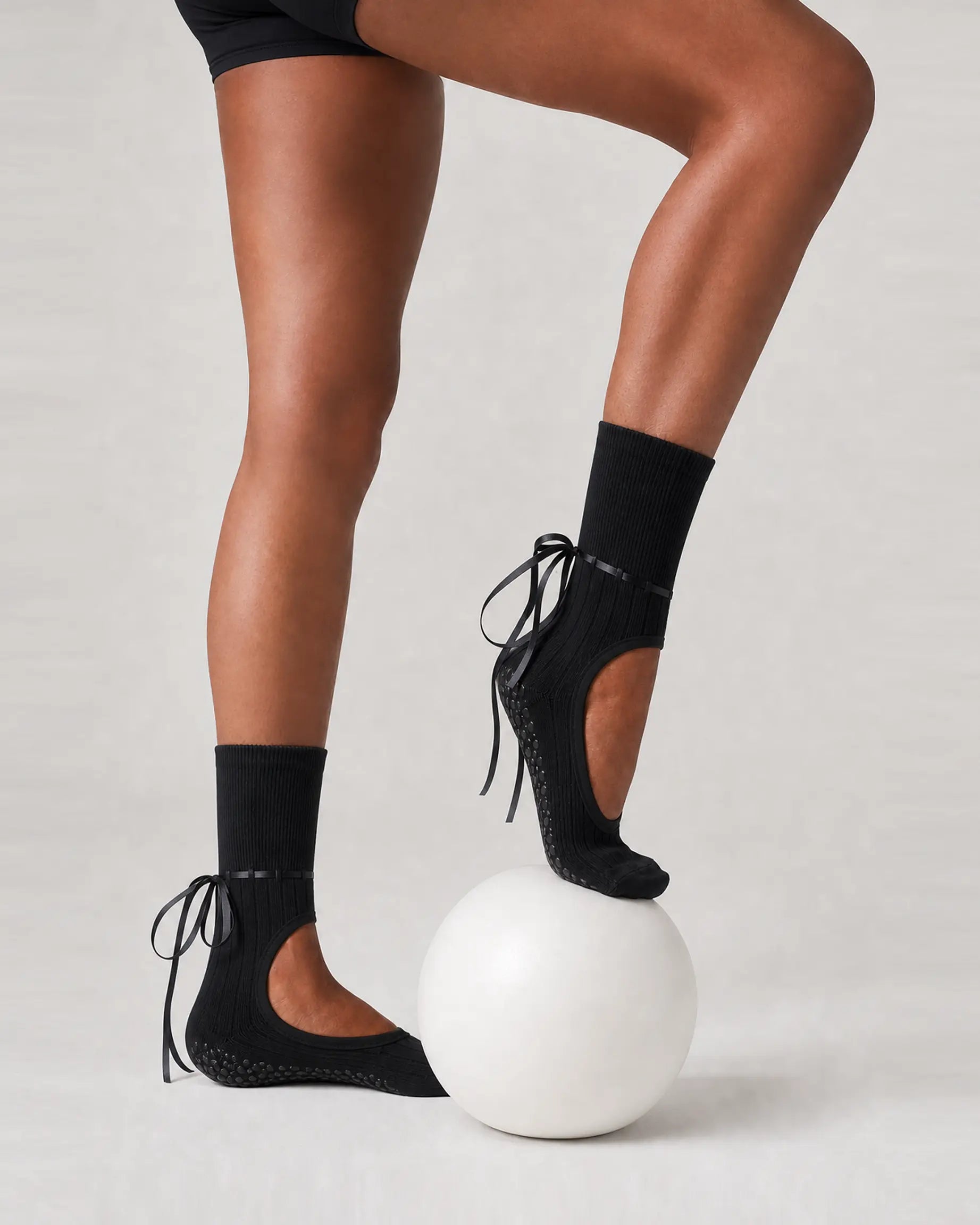 black | 03 | Black ribbon-tie open-instep grip socks exercise ball pose showing the ballet-inspired shape, crew coverage, and above-ankle ties