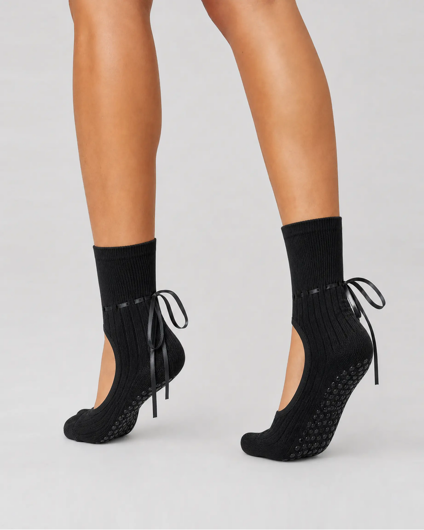 black | 04 | Black ribbon-tie open-instep grip socks side angled pointed standing view showing the covered heels, open insteps, and ribbon-tie details
