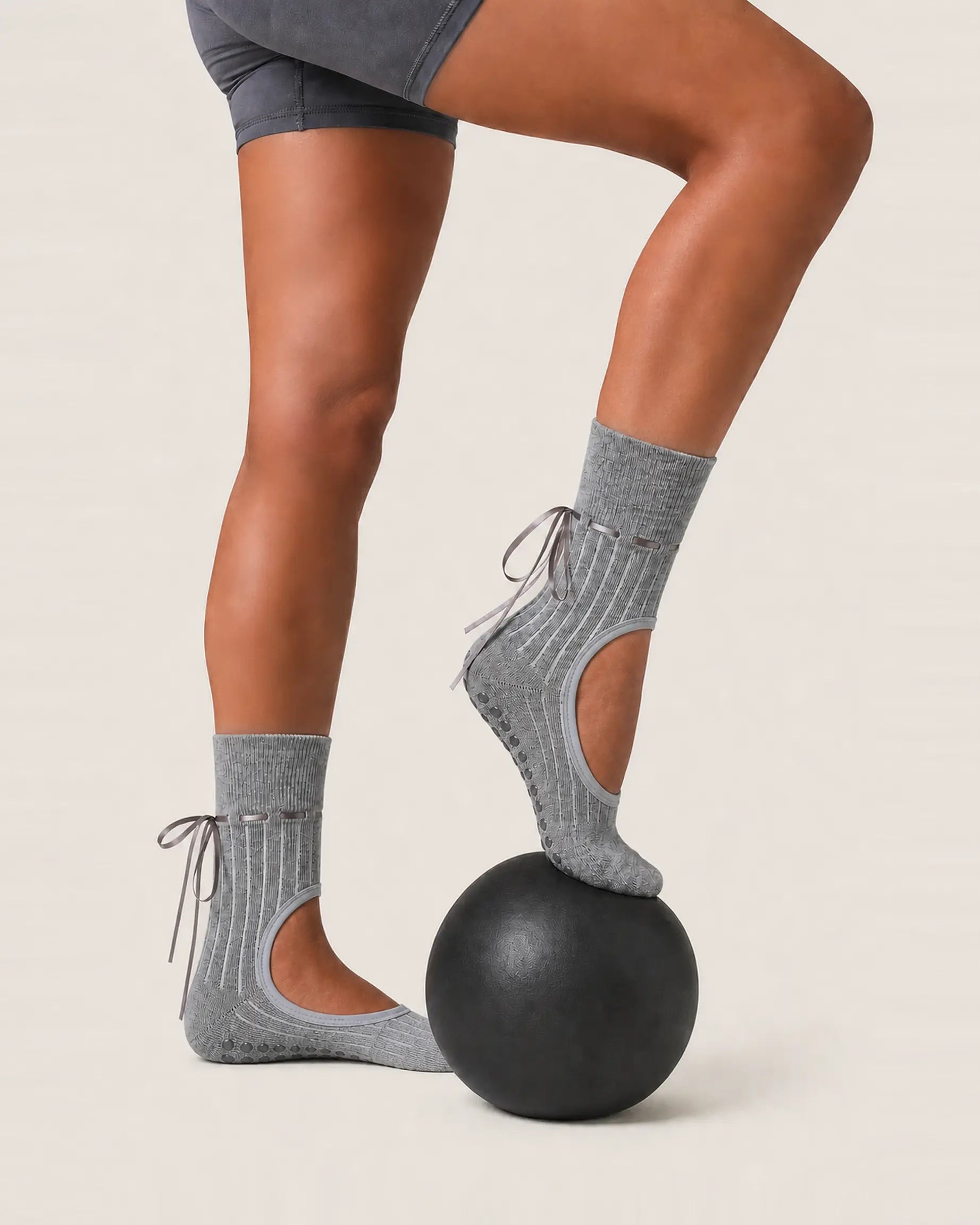grey | 03 | Grey ribbon-tie open-instep grip socks exercise ball pose showing the ballet-inspired shape, crew coverage, and above-ankle ties